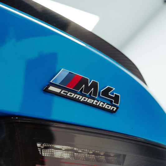 Gloss black rear model badge for BMW M4 Competition, featuring silver edging and the M4 Competition logo. Genuine BMW