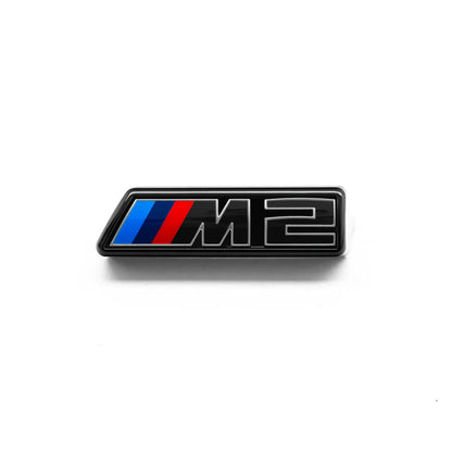 Gloss black front grille emblem with silver outline and the letters 'M2' for a BMW vehicle.